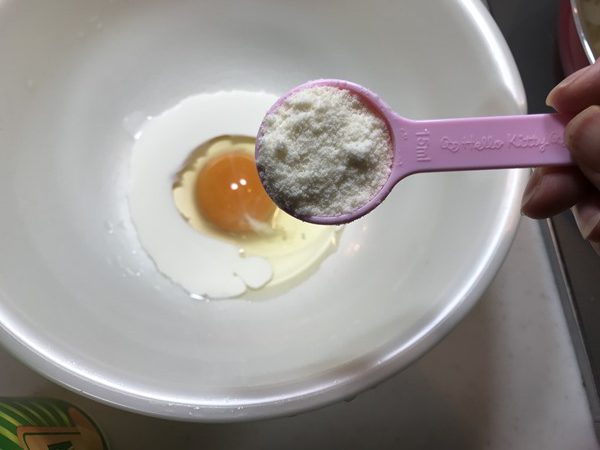 卵と生クリームが入ったボウルに業務スーパーの粉チーズを加えるところ