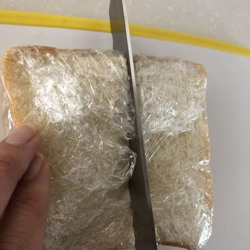 具材を挟みラップに包んだパンを切る様子