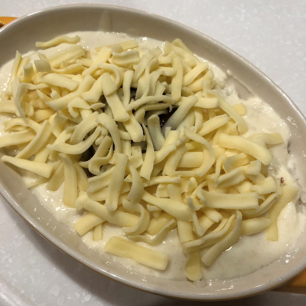 ハンバーグの上にホワイトソースとチーズをかける