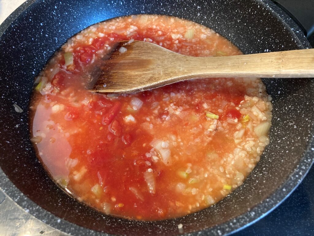 炒めた米などにカットトマト缶と水を入れて炒める