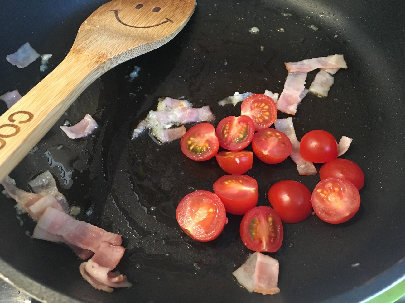 オリーブオイルを熱したフライパンでベーコンとトマトに火を通す