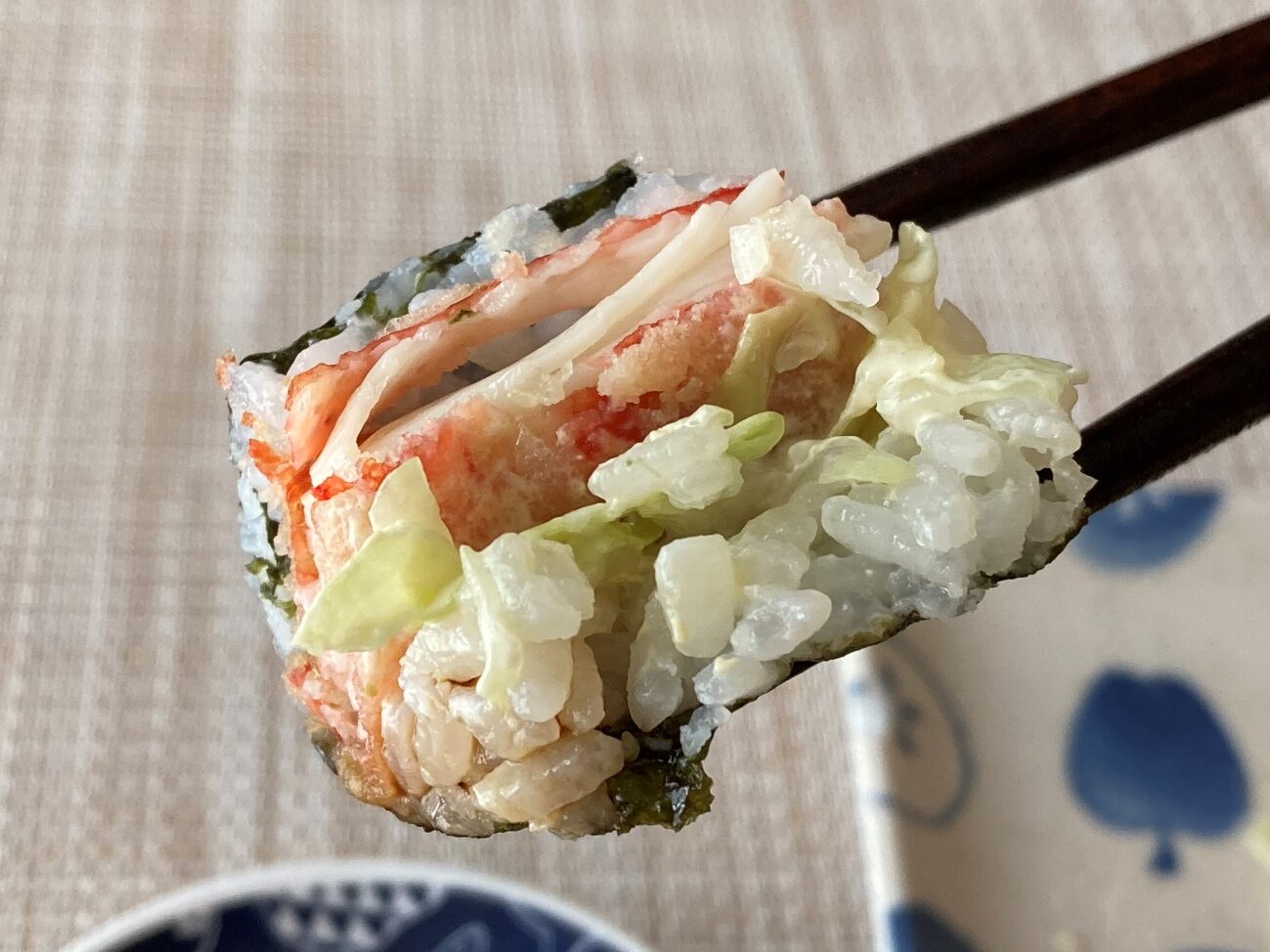 箸で持ち上げた業務スーパーのかにかま棒身天ぷらで作った巻き寿司のアップ