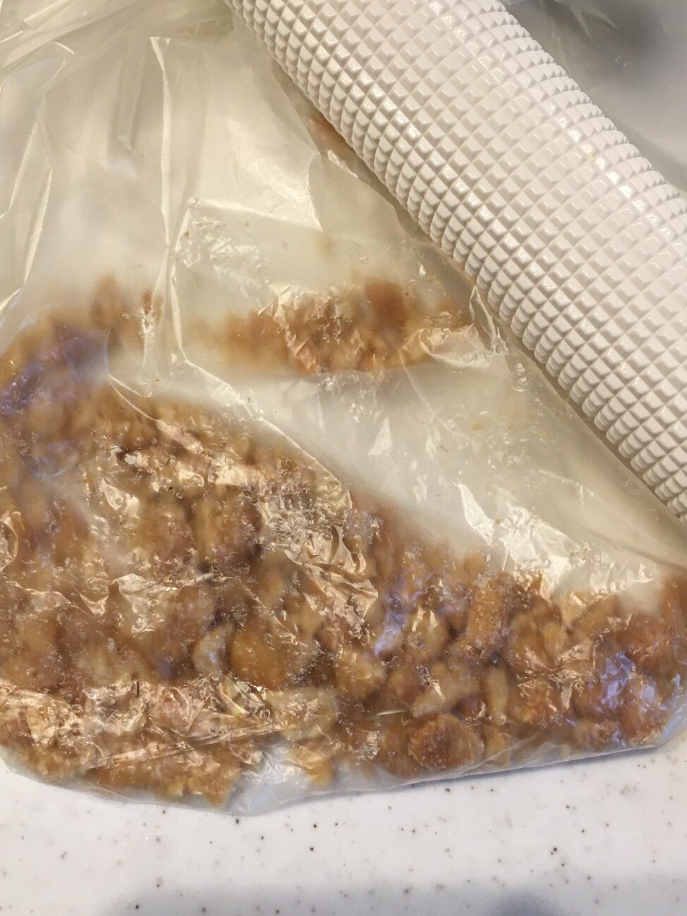 透明袋に入れた業務スーパーのハニーローストピーナッツを麺棒で粗く砕く