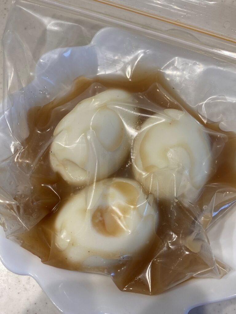 レンジ加熱した残りの業務スーパーの鶏白湯しょうゆ鍋つゆと殻をむいたゆで玉子を別の密閉袋に入れる