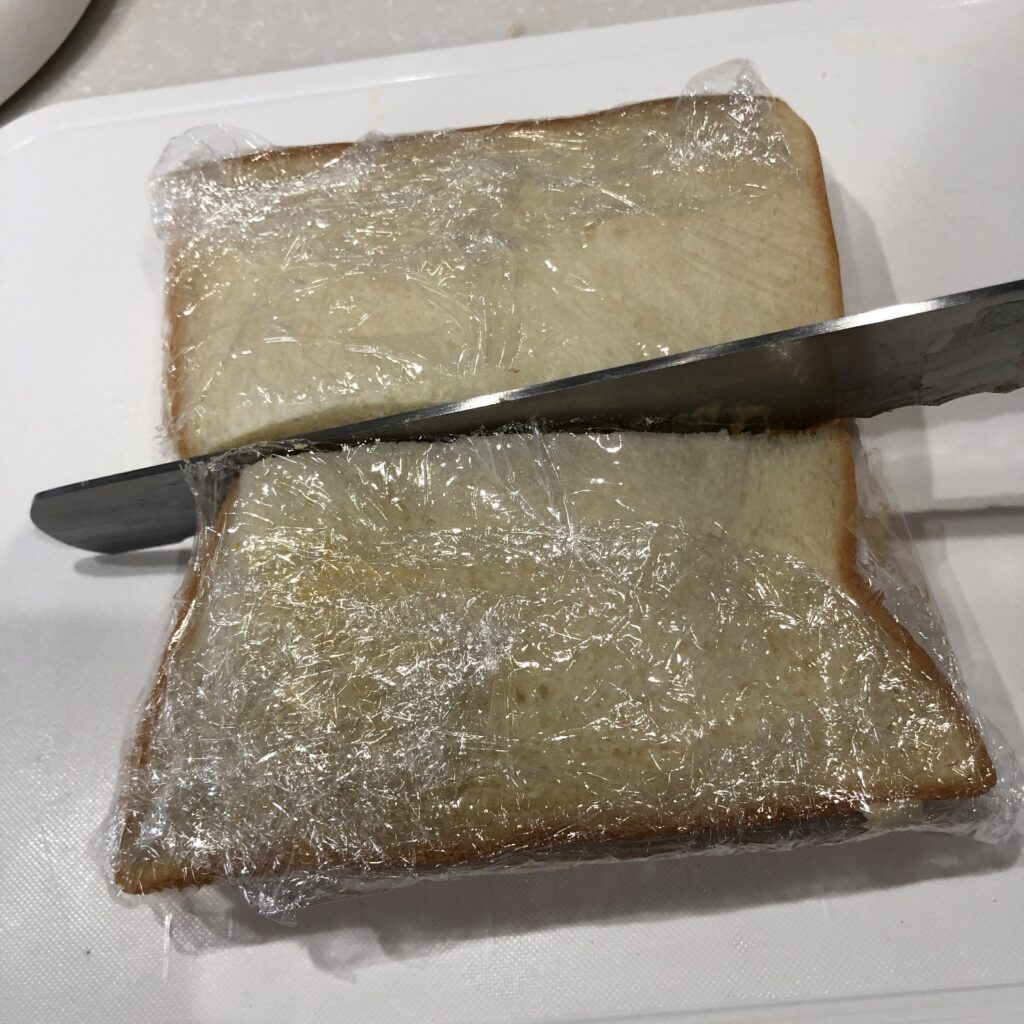 もう1枚のパンを重ねてラップで包み、ラップの上から切る　