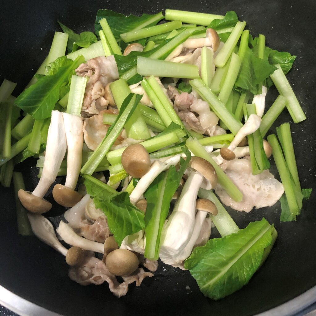 ごま油で豚肉を炒め、小松菜の茎部分としめじを加える