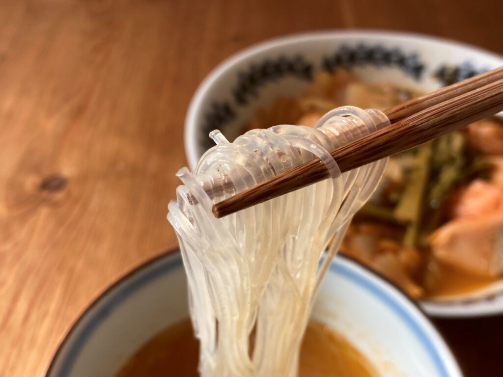 箸で持ち上げた業務スーパーのトムヤム鍋の素で作ったトムヤム鍋スープで煮た春雨のアップ