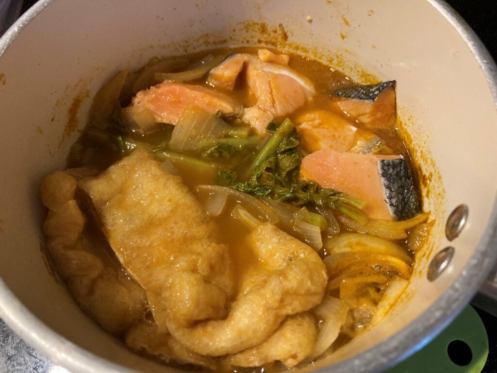 鍋に入れた業務スーパーのトムヤム鍋の素・鮭・油揚げ・大根の葉・玉ねぎ